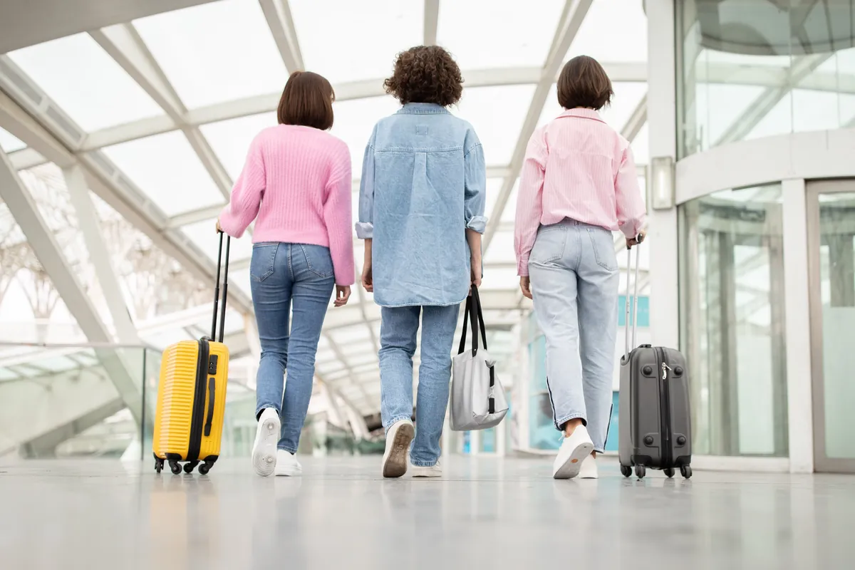 Three travellers walking with suitcases through a bright glass airport terminal