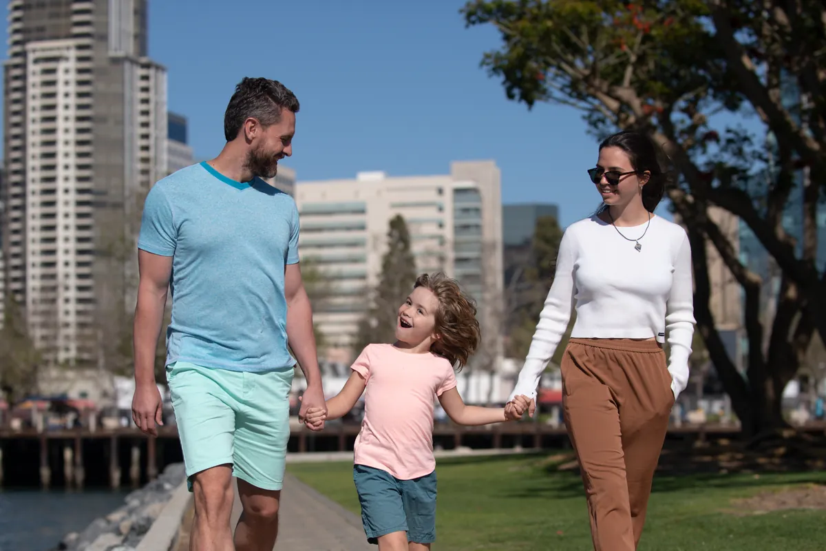Family holding hands walking through a city park with towers behind