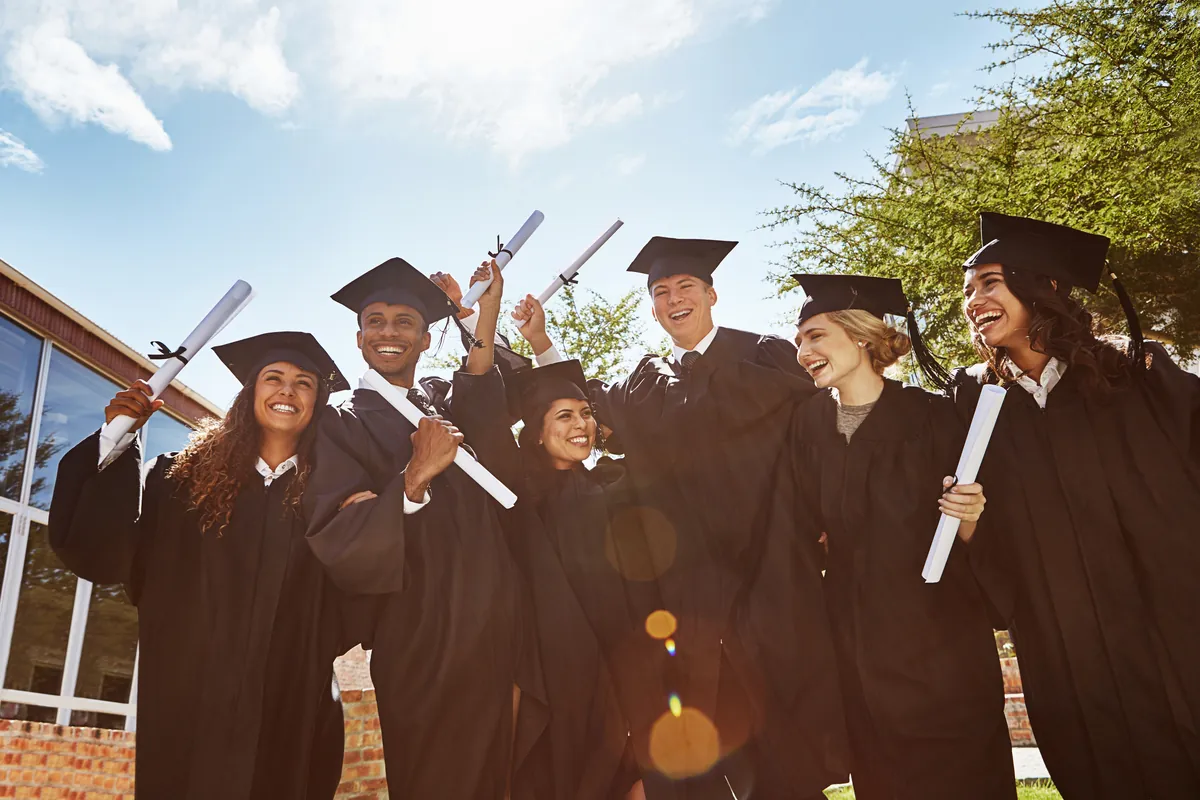 Diverse graduates in gowns and caps celebrating outdoors in sunshine