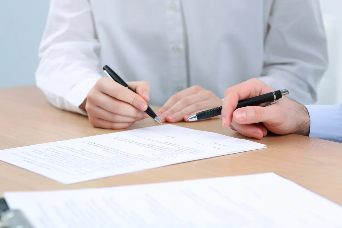 Close-up of hands signing an agreement with pens on a bright desk