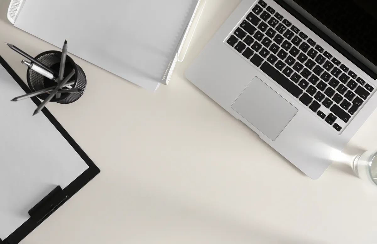 Top-down view of a laptop, clipboard and pens on a clean white desk
