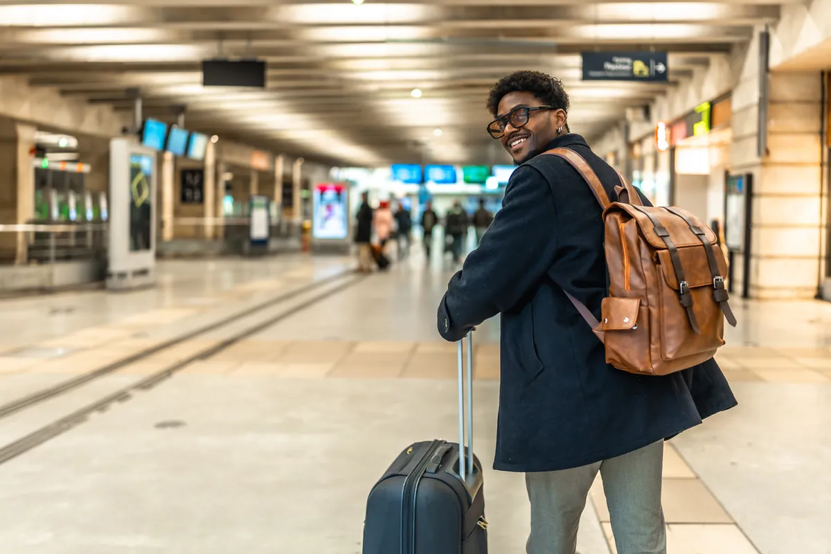 Smiling young traveller with a backpack and suitcase in a bright airport terminal