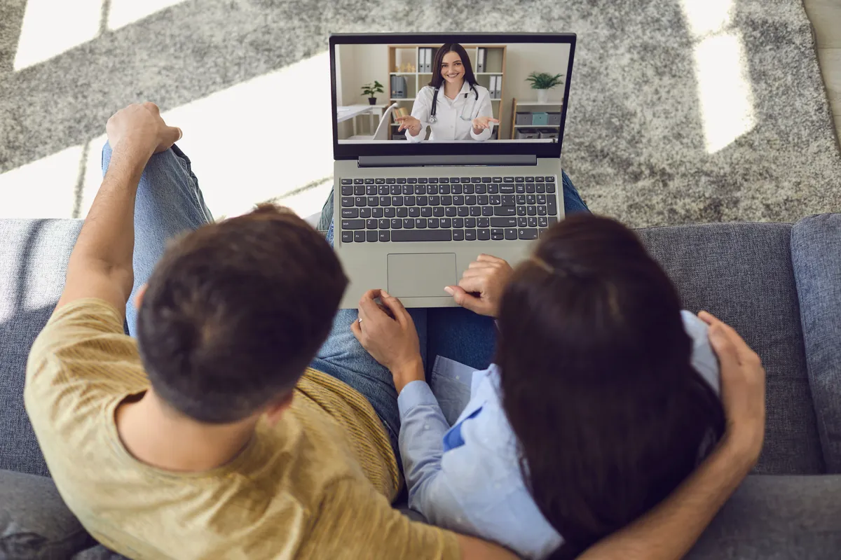 Couple on a sofa at home talking with an adviser on a laptop video call